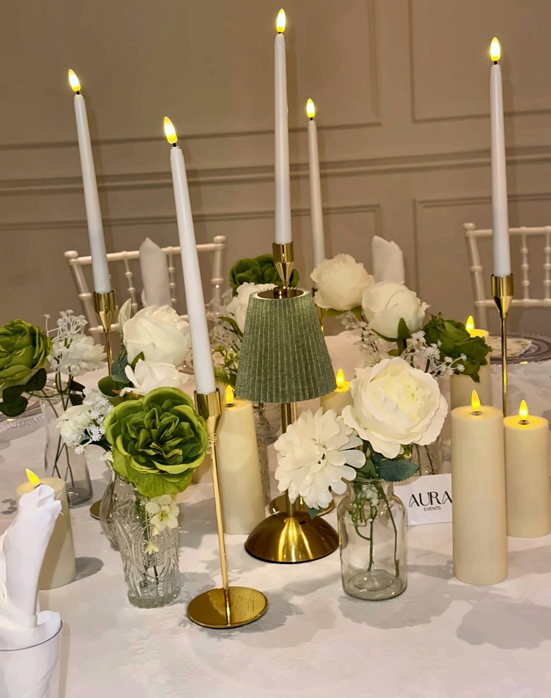 Tall candles, peonies and a pleated lamp on a dinner table