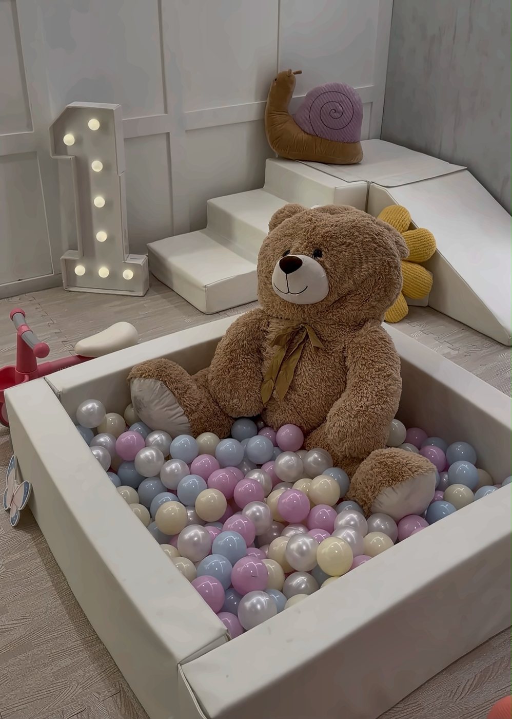 A giant teddy in a pastel ball pit beside a lit number one