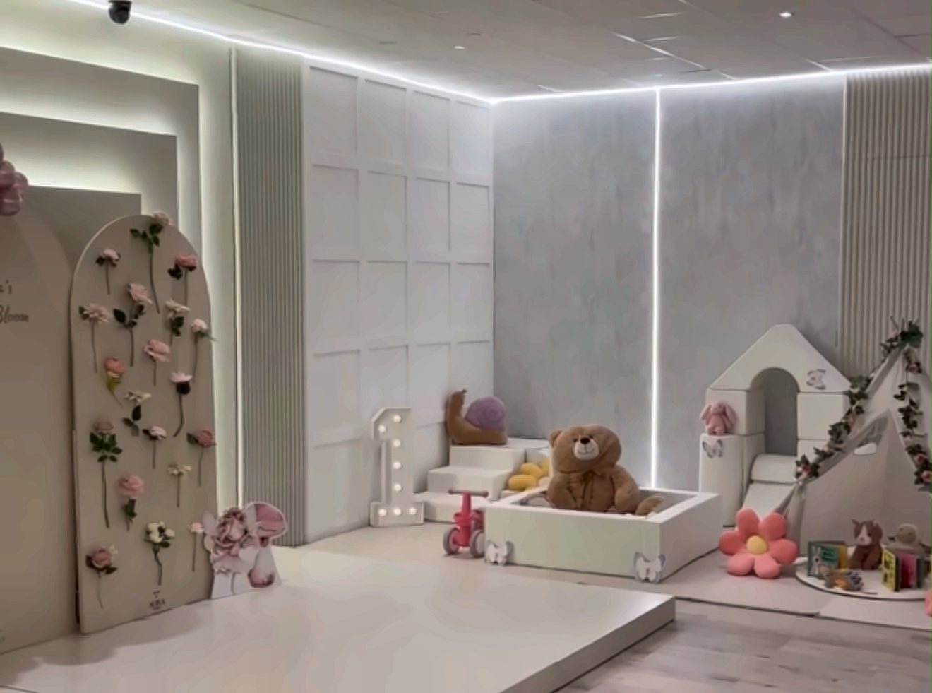 A soft-play corner with a ball pit, a giant teddy, a tepee and a flower wall, set for a first birthday
