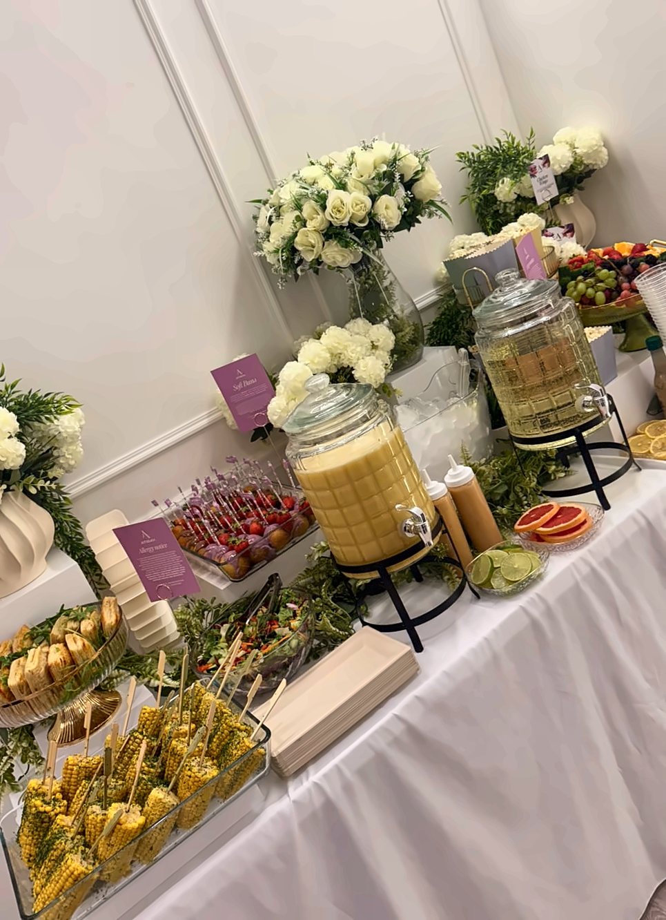 A grazing table with drinks dispensers, fruit and florals