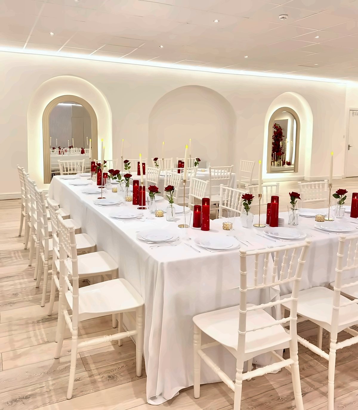 A long white dinner table with red roses and red candles under the lit arches