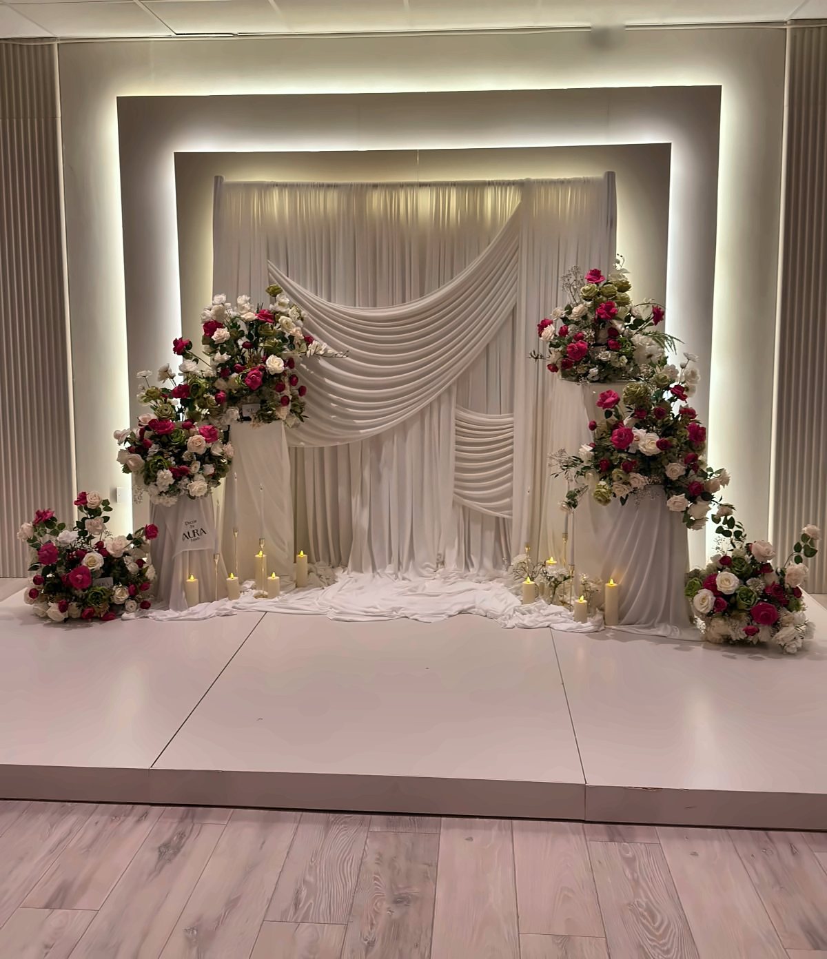 A white draped backdrop on the lit stage at The XL Suite, dressed with pink and white roses and candles
